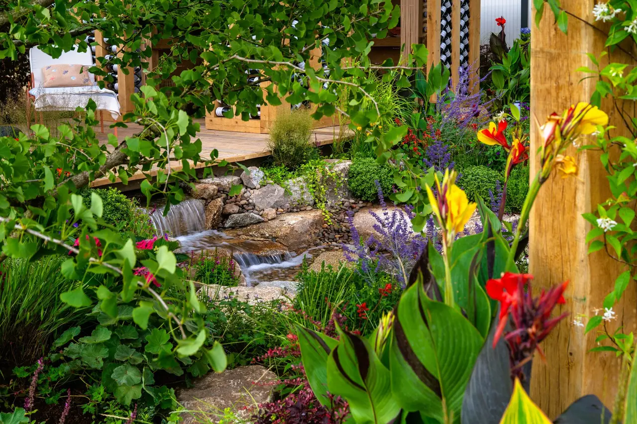 Naturalistic waterfall framed by lush colourful planting in the 100 Sweet Summers show garden